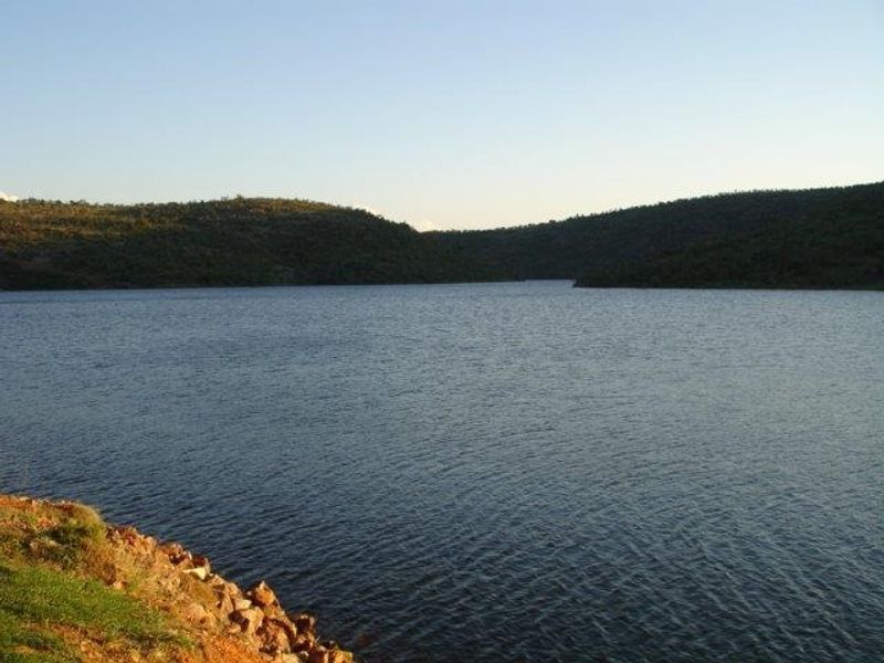 A scenic view of a large lake surrounded by rolling hills and natural vegetation.