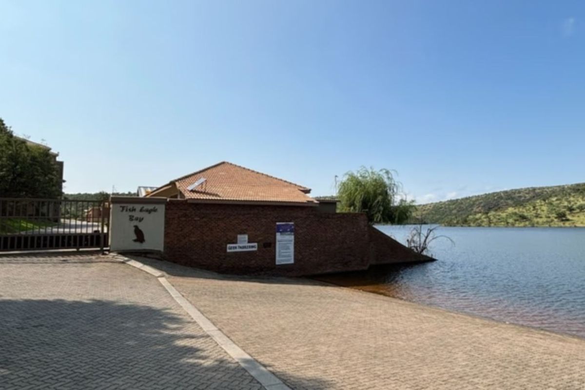 Entrance view of the property featuring a paved driveway, security gate, and direct access to the waterfront.