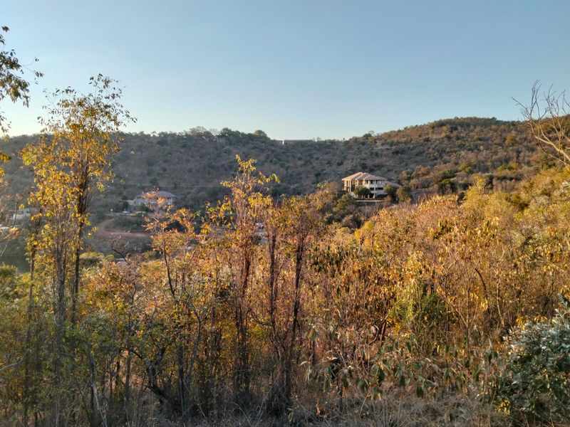 A scenic landscape view overlooking natural bushveld terrain with distant residential properties nestled into the hillside.