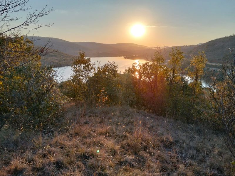 A scenic sunset view overlooking a tranquil lake surrounded by rolling hills and natural vegetation on the residential land.