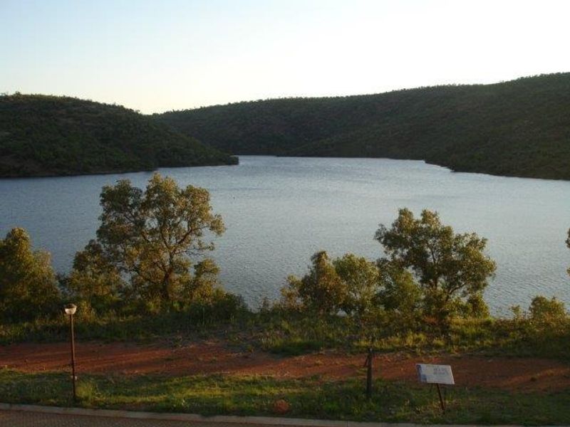 A scenic view overlooking a large dam or lake surrounded by natural hills and vegetation.