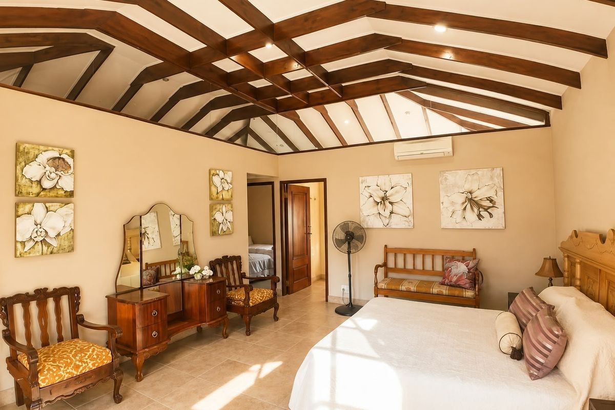 Spacious bedroom featuring high vaulted ceilings with exposed timber beams, tiled flooring, and a wall-mounted air conditioning unit.