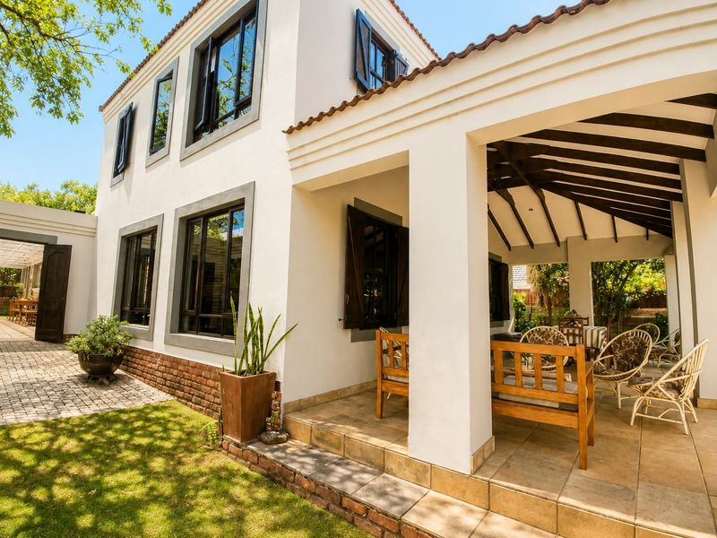 A well-maintained rear exterior view featuring a covered patio with exposed timber rafters, tiled flooring, and classic casement windows with shutters.