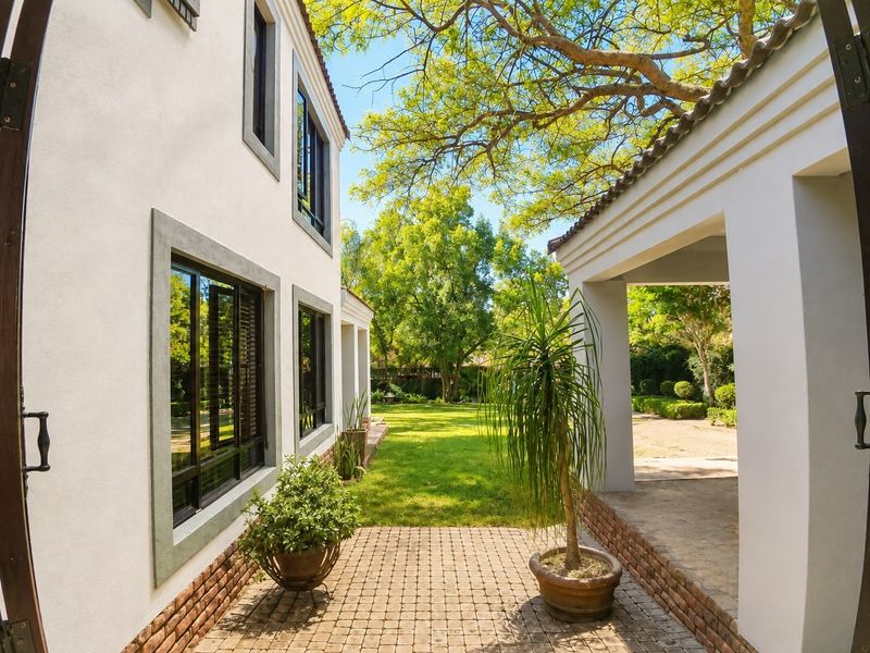 A well-maintained rear exterior view featuring a paved patio area, covered walkway, and a lush, landscaped garden with mature trees.