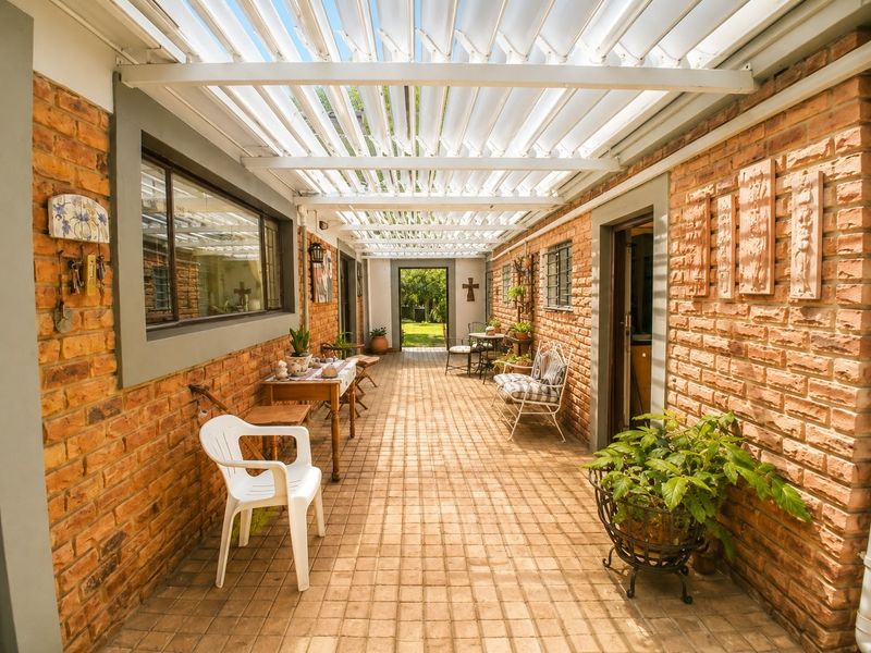 Covered outdoor patio featuring exposed brick walls and a louvred pergola roof, providing a sheltered transition space between the home and the garden.