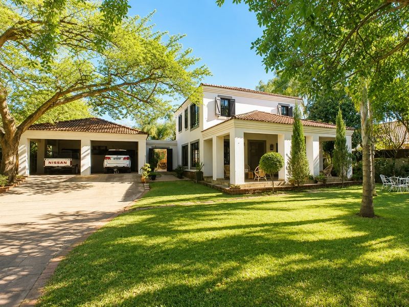 A well-maintained two-story house featuring a covered patio, double garage, paved driveway, and a lush, landscaped front garden.