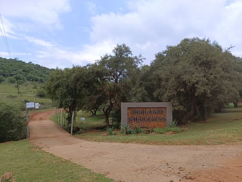 Entrance view of the Highlands Wilderness estate, featuring a prominent stone-clad signage wall, dirt access road, and natural landscape surroundings.