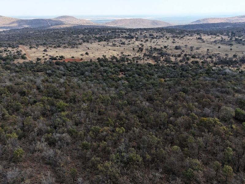 An aerial view of a vast, undeveloped residential land parcel featuring dense native bushveld and rolling hills in the distance.