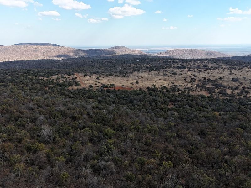 An aerial view of expansive vacant residential land featuring native bushveld vegetation and distant mountain range vistas.