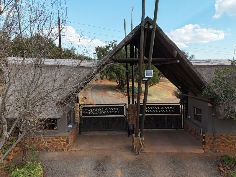 The main entrance gate to Highlands Wilderness, featuring a rustic thatched roof structure, stone masonry, and secure gated access.
