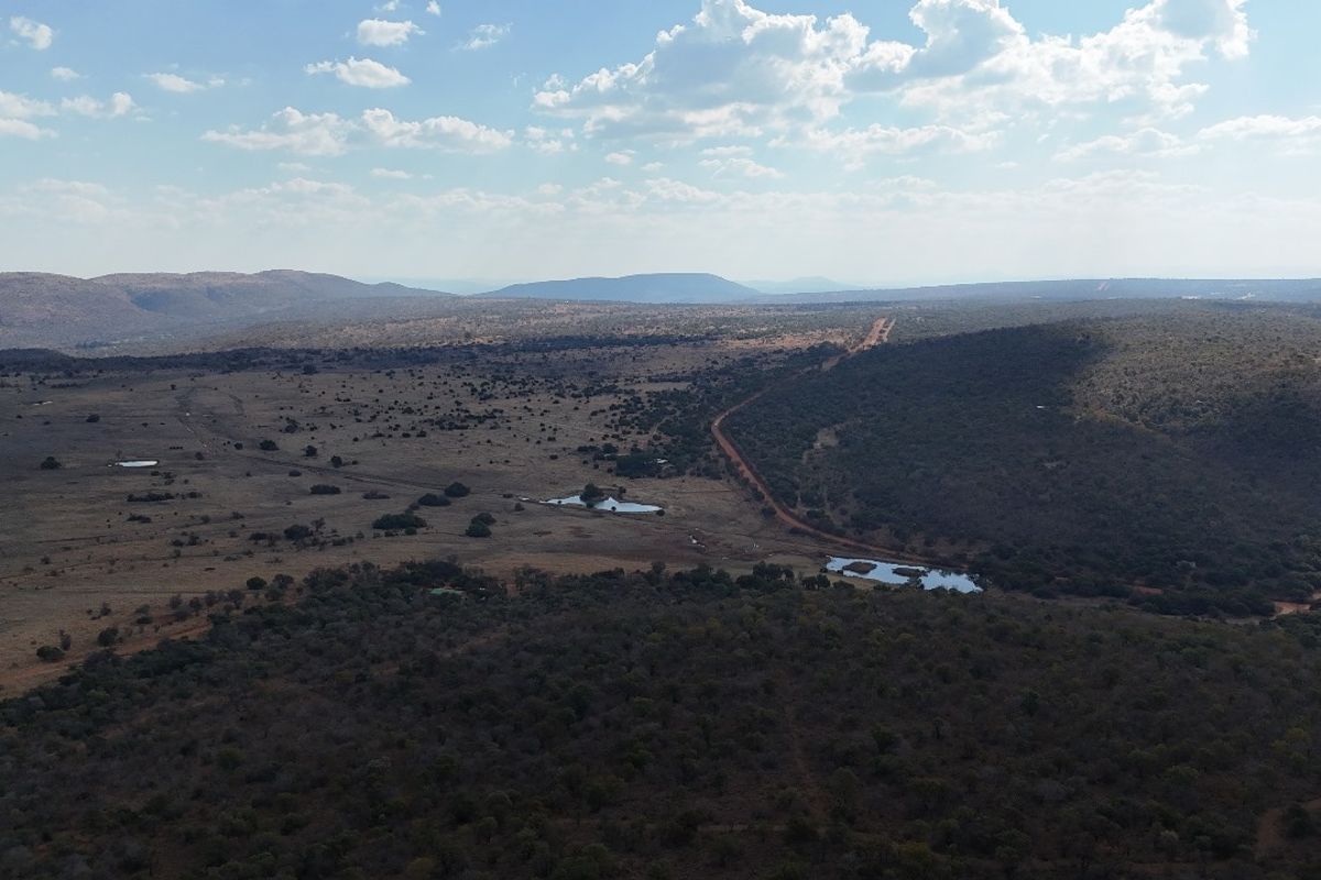 An aerial view of a vast, undeveloped residential land parcel featuring natural vegetation, dirt access roads, and small water features.