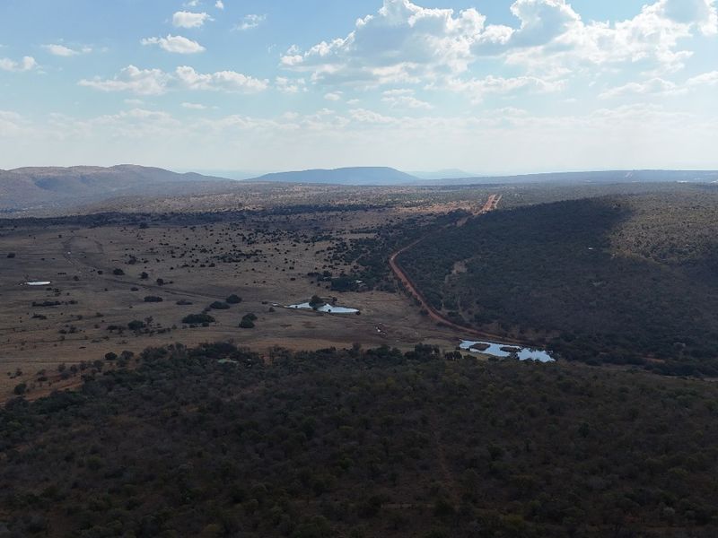 An aerial view of a vast, undeveloped residential land parcel featuring natural vegetation, dirt access roads, and small water features.