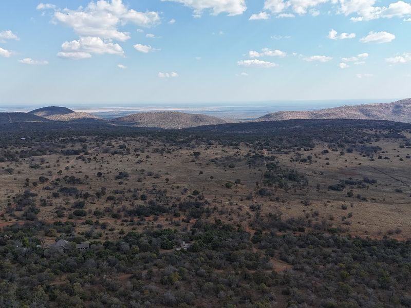 An expansive aerial view of the vacant residential land, showcasing the natural landscape, surrounding vegetation, and distant mountain ranges.