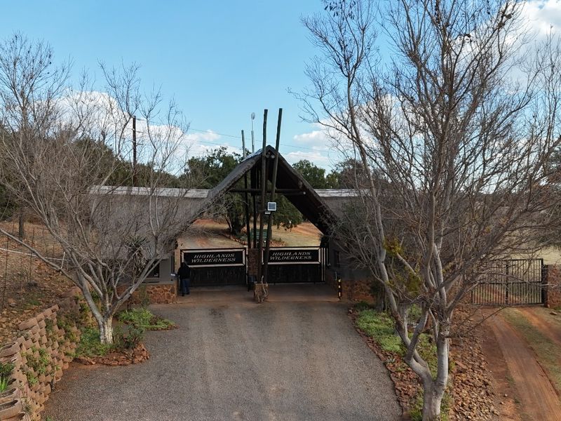 Aerial view of the Highlands Wilderness estate entrance featuring a secure gated access point with a thatched roof structure and perimeter fencing.