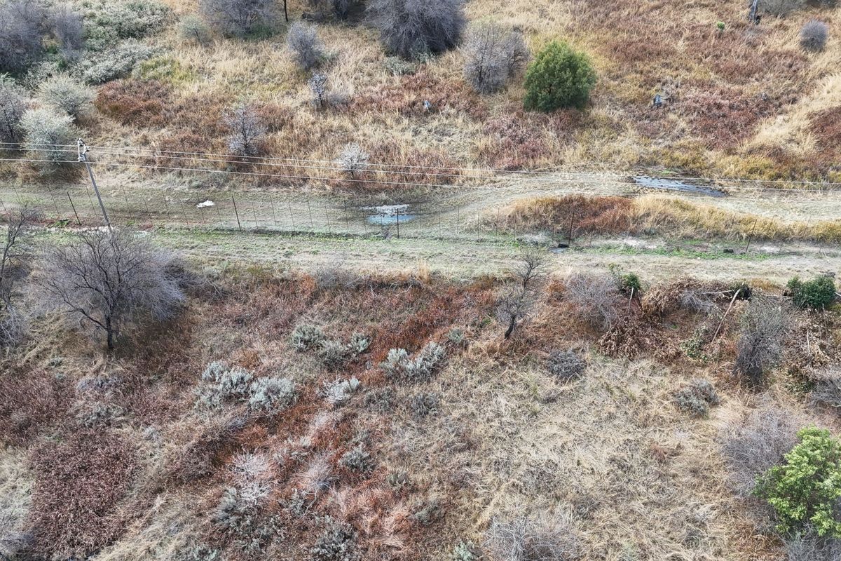 An aerial view of a vacant residential plot featuring natural vegetation, perimeter fencing, and overhead power lines.