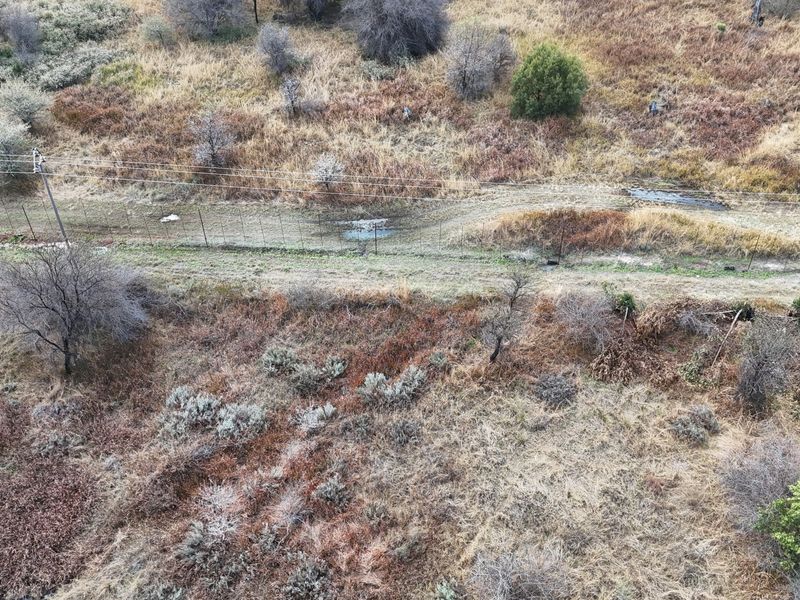 An aerial view of a vacant residential plot featuring natural vegetation, perimeter fencing, and overhead power lines.