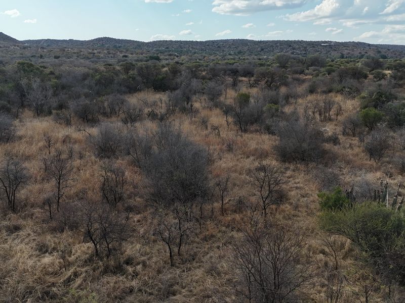 An aerial view of a large, undeveloped residential land plot featuring natural bushveld vegetation and distant hilly terrain.