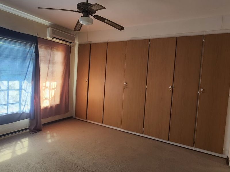 A spacious bedroom featuring extensive built-in wooden cupboards, a ceiling fan, and a wall-mounted air conditioning unit.