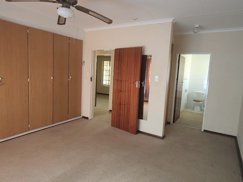 Spacious bedroom featuring extensive built-in cupboards, a ceiling fan, and direct access to an en-suite bathroom.