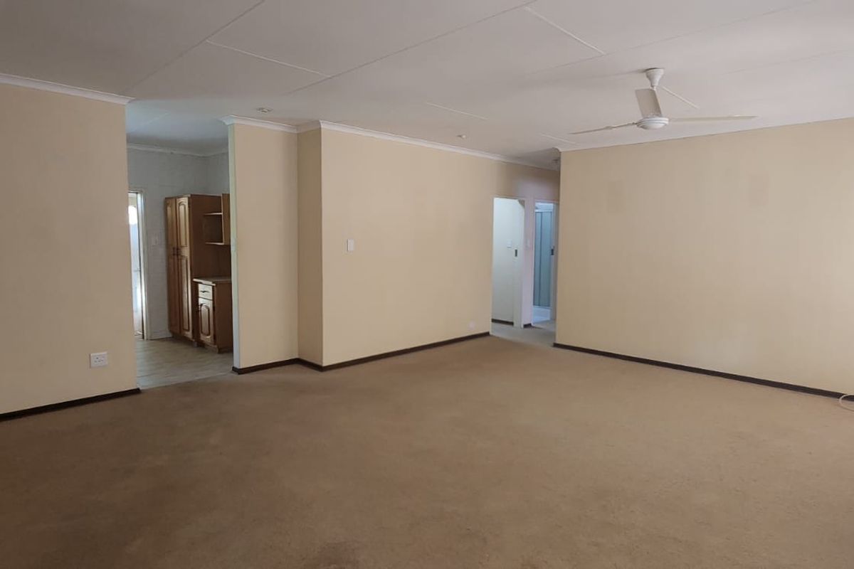 A spacious, empty living area featuring neutral walls, carpeted flooring, and a ceiling fan, offering a blank canvas for interior design.