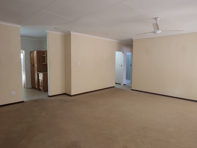 A spacious, empty living area featuring neutral walls, carpeted flooring, and a ceiling fan, offering a blank canvas for interior design.