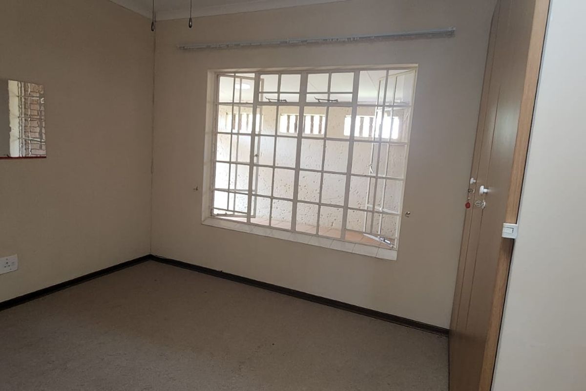 An empty bedroom featuring built-in wardrobes, carpet flooring, and security bars on the window, offering a blank canvas for renovation.