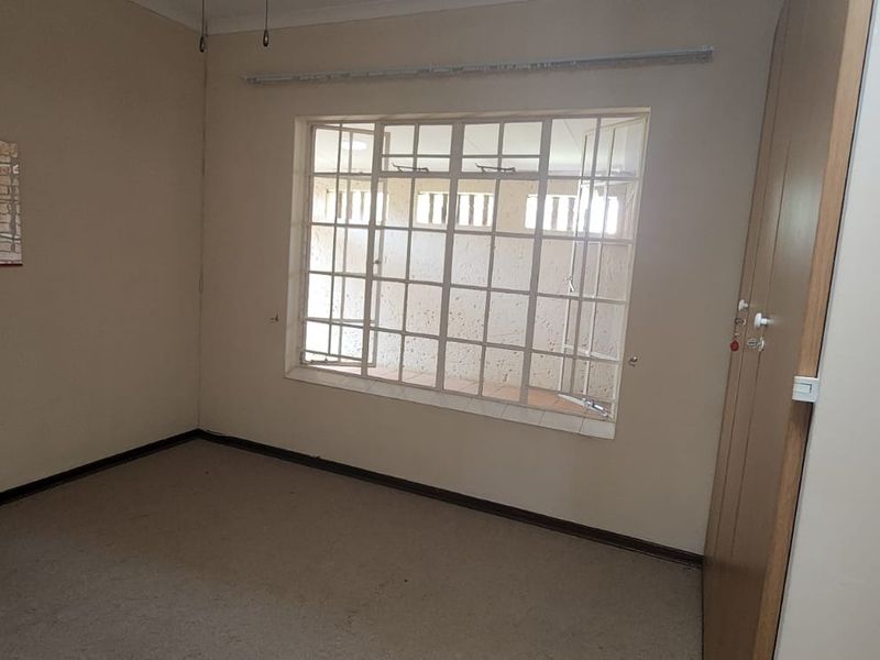 An empty bedroom featuring built-in wardrobes, carpet flooring, and security bars on the window, offering a blank canvas for renovation.