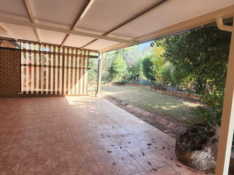 A spacious covered patio featuring tiled flooring and a brick facade, overlooking a private garden area, ideal for outdoor relaxation and entertainment.