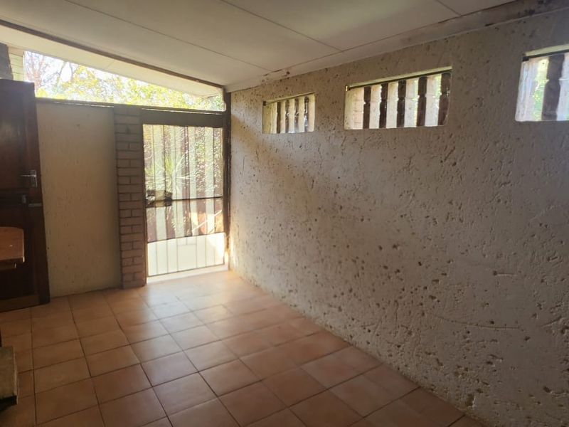 A covered patio area featuring tiled flooring, textured walls, and high-level windows, offering a functional outdoor space with potential for modernization.