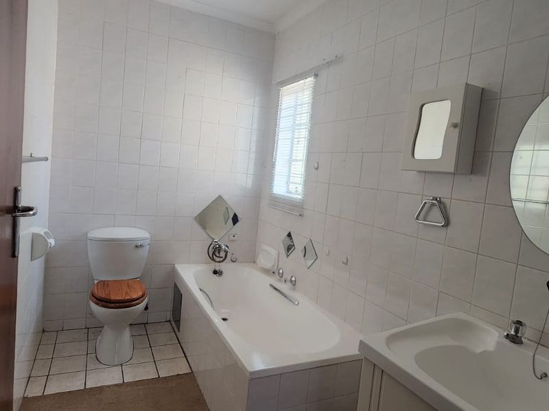 A dated bathroom featuring a built-in bathtub, vanity basin, and toilet, finished with full-height ceramic wall tiling.