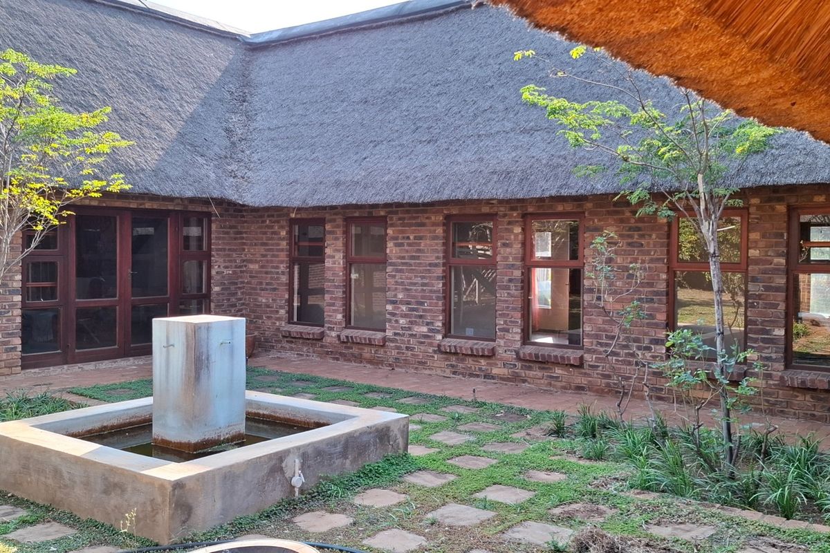 A rear courtyard featuring a traditional thatched roof, exposed brick walls, timber-framed windows, and a central concrete water feature set within brick paving.