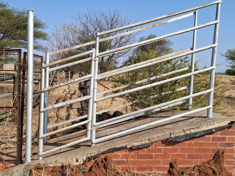 A functional livestock loading ramp featuring a concrete surface, steel fencing, and a brick foundation, situated in an open farm environment.