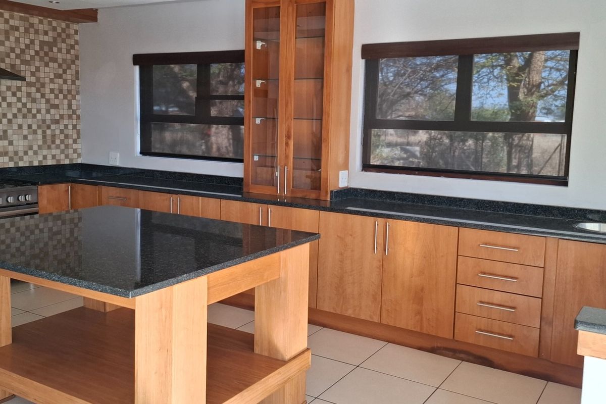 A well-maintained kitchen featuring wooden cabinetry, granite countertops, a central island, and a stainless steel gas stove with a mosaic tile backsplash.