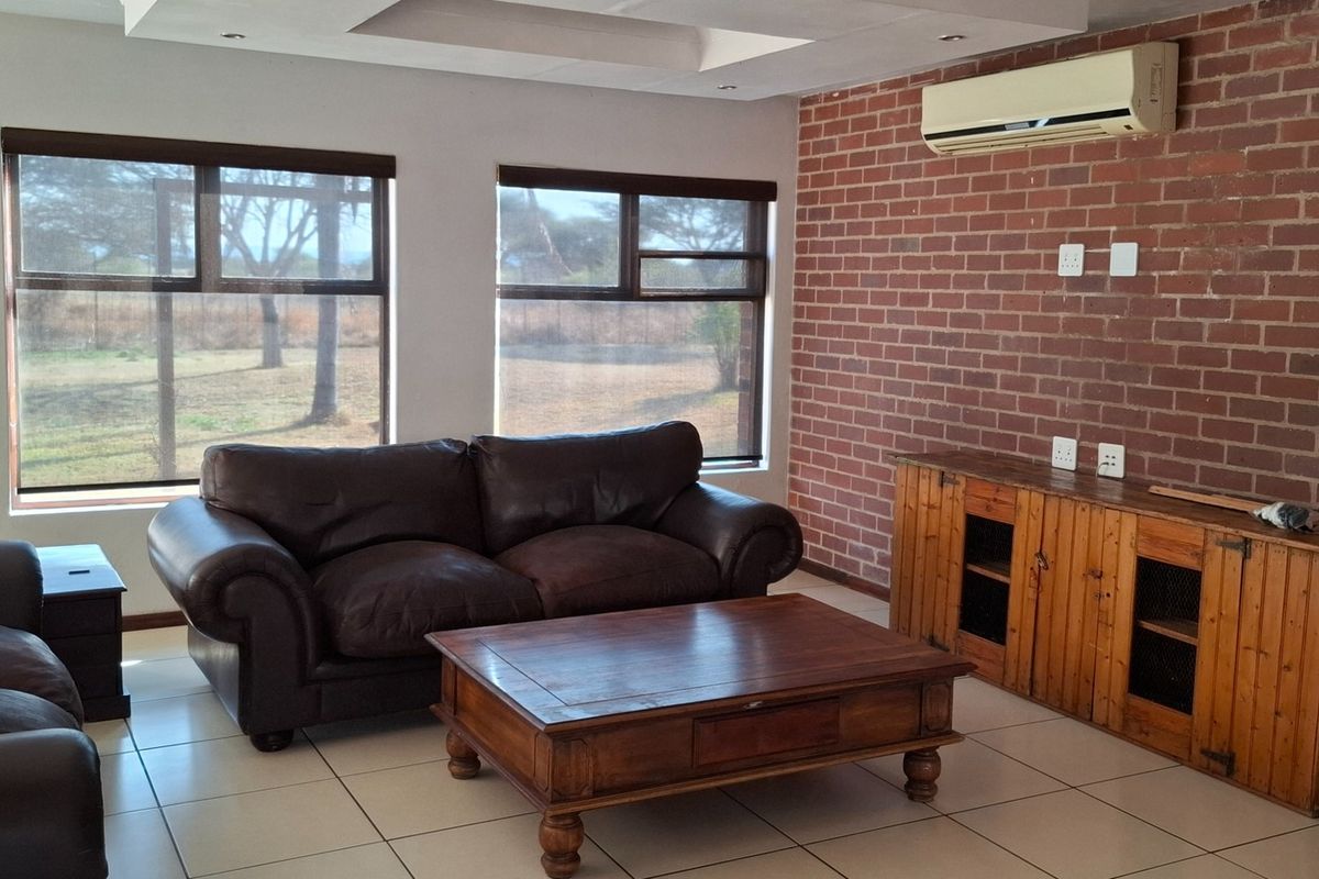 A living room featuring an exposed brick feature wall, tiled flooring, recessed ceiling lighting, and a wall-mounted air conditioning unit.