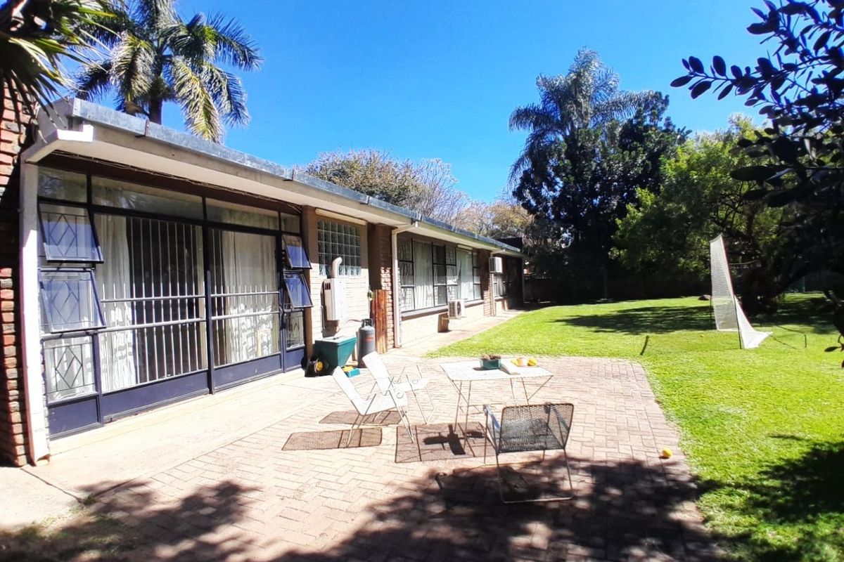 Rear view of the property featuring a brick-paved patio area, large sliding doors with security bars, and a spacious garden.