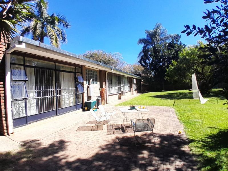 Rear view of the property featuring a brick-paved patio area, large sliding doors with security bars, and a spacious garden.