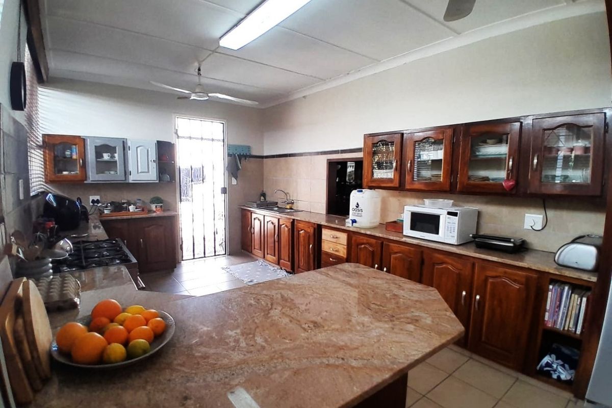 Spacious kitchen featuring extensive wooden cabinetry, stone countertops, gas hob, and direct access to the exterior via a security gate.
