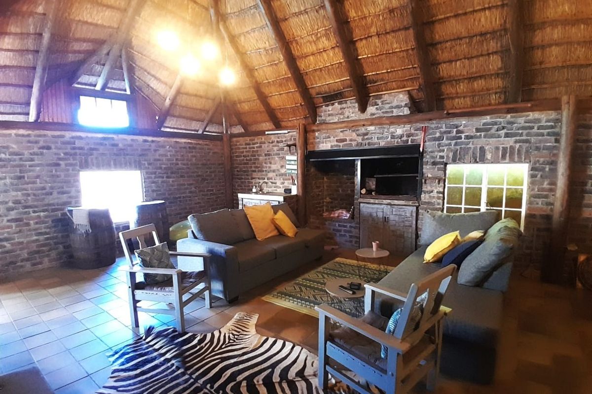 Spacious living area featuring a rustic thatched roof, exposed timber rafters, and a traditional brick fireplace, creating a warm and character-filled atmosphere.