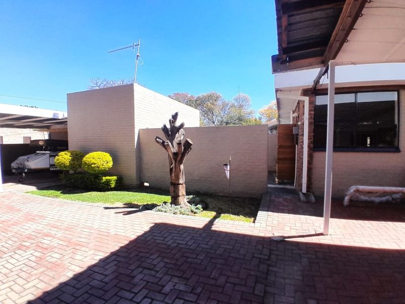 A paved rear courtyard area featuring a covered patio, boundary wall, and a carport structure.