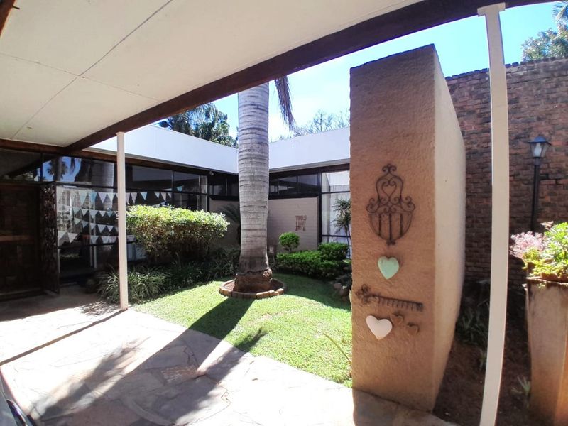 A covered patio area overlooking a private courtyard garden with established palm tree and brick wall features.