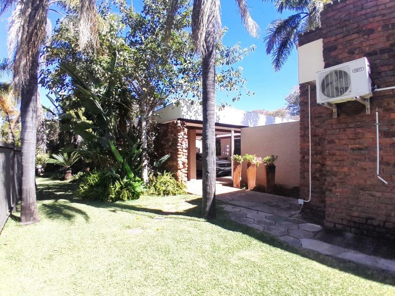 Rear exterior view featuring a landscaped garden, paved walkway, and exposed brick wall with an integrated air conditioning unit.