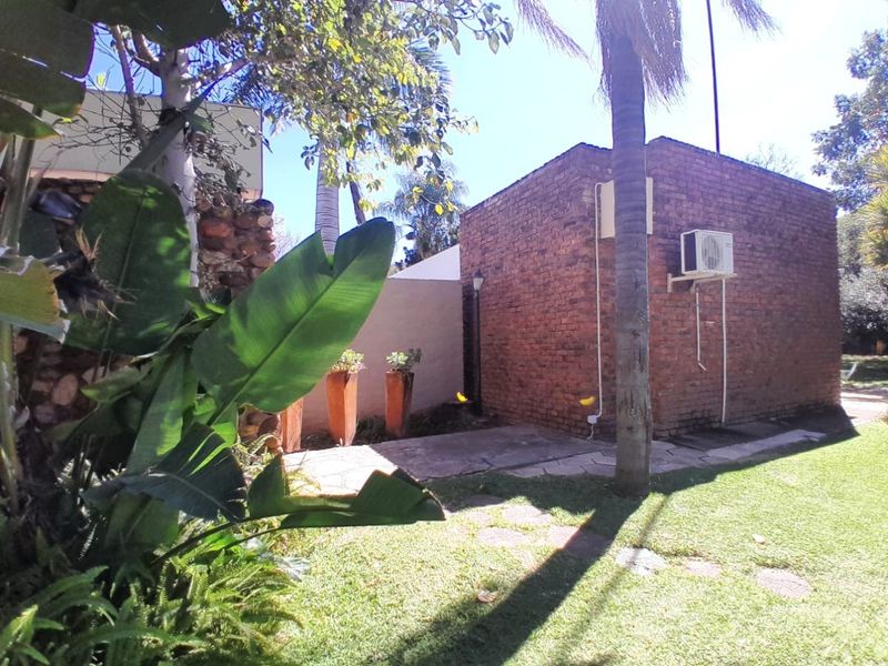 A view of the rear exterior featuring an exposed brick wall, an installed air conditioning unit, and a landscaped garden area with a paved path.