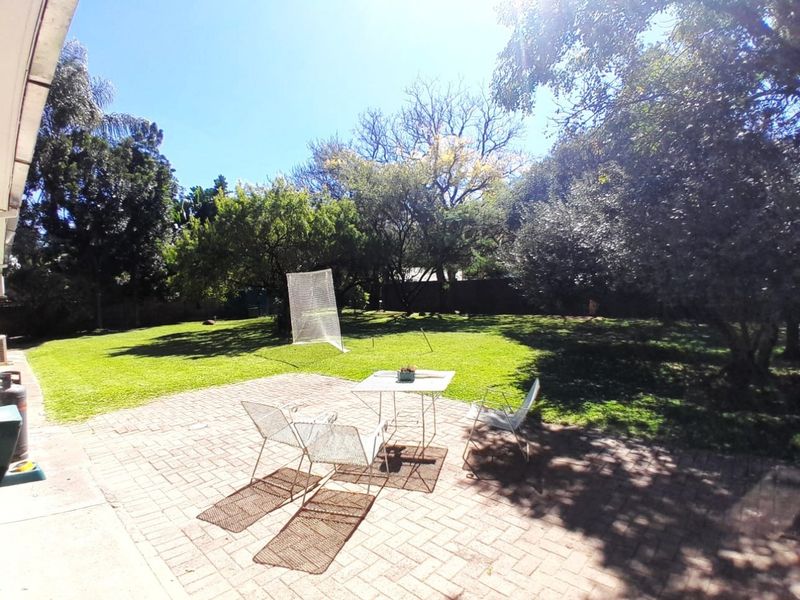 A spacious rear garden featuring a paved patio area and a well-maintained lawn surrounded by mature trees.
