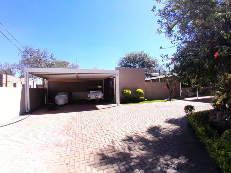 A spacious paved driveway leading to a covered carport area, featuring brick boundary walls and established garden landscaping.