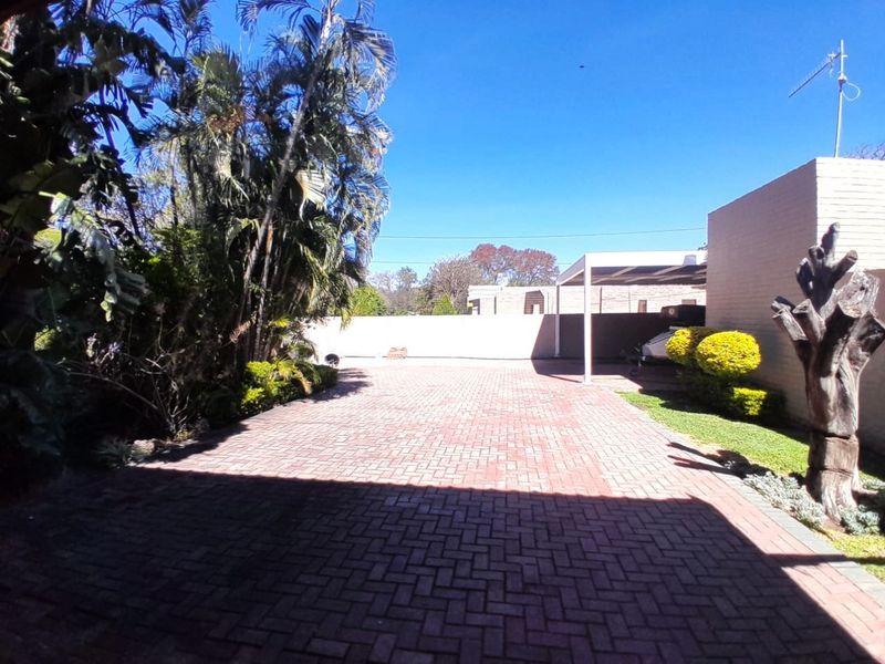 A spacious paved driveway leading to a carport, featuring established garden landscaping and secure boundary walls.