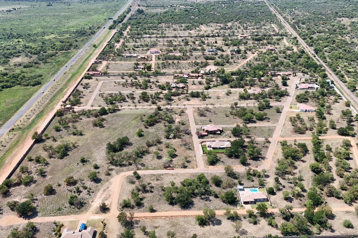 An aerial view of a residential estate development featuring established plots, internal road networks, and surrounding natural landscape.
