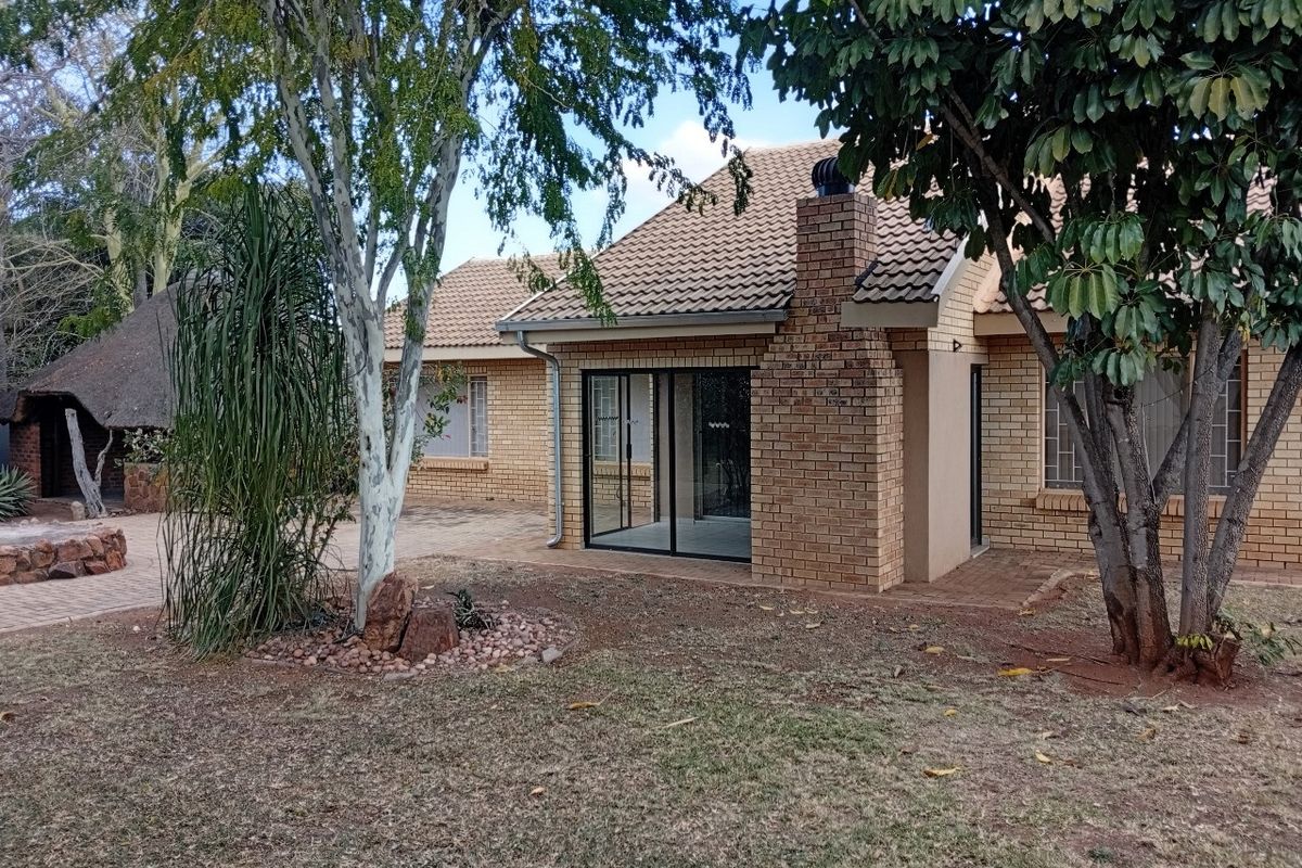 Rear view of a brick house featuring a tiled roof, brick chimney, sliding glass doors leading to a paved patio, and a separate thatched lapa.