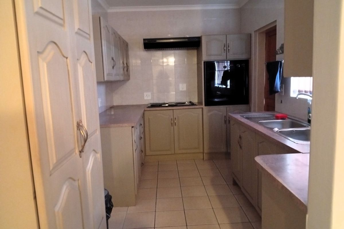 A functional kitchen featuring built-in cabinetry, laminate countertops, a built-in oven, hob, extractor fan, and a double bowl sink with tiled flooring.