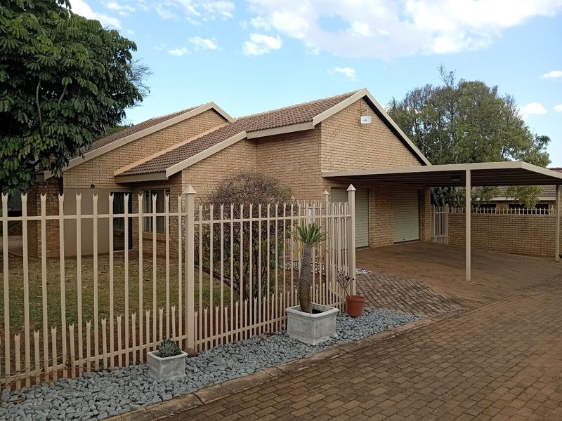 Front view of a face brick house featuring a paved driveway, double carport, and secure metal perimeter fencing.