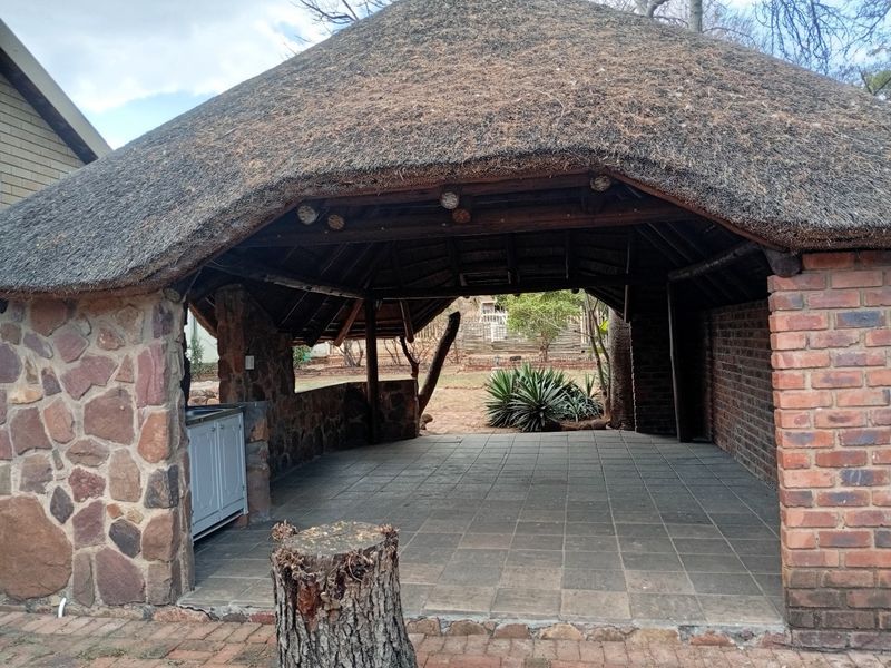 An outdoor thatched lapa area featuring stone and brick construction, tiled flooring, and built-in cabinetry, overlooking the garden.